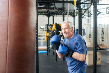 Handsome senior male training with punching bag. Old trainer training with punching bag in fitness studio. People, sport, active way of life.