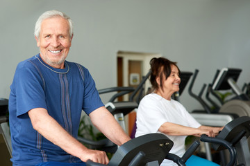 Happy elderly man working out in gym. Smiling caucasian pensioner looking at camera while training at gym. Sport and seniors.