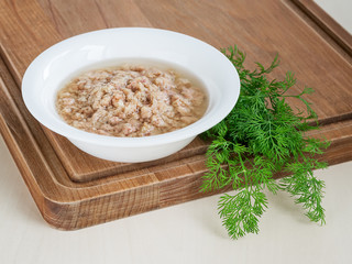 White bowl with shredded tuna in oil for cooking salad and green dill on a wooden background. Seafood, healthy eating and cook at home.