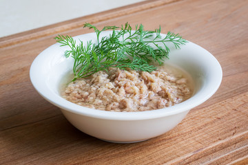 White porcelain bowl with shredded tuna in oil for a salad and green dill on a wooden background. Seafood, healthy eating and cook at home.