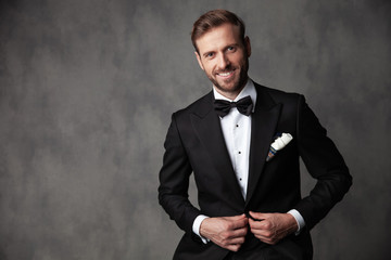 Jolly groom standing and fixind his tuxedo