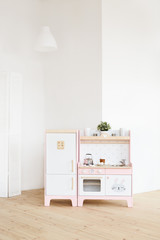 Play furniture for children. Wooden pink and white kitchen with fridge, stove, oven and sink in big light room