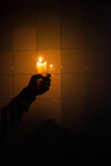 Hand holding the candle against the tiled wall
