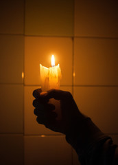 Hand holding the candle against the tiled wall