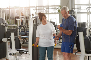 Fototapeta na wymiar Elderly couple working out at gym. Senior man lifting dumbbells at fitness center. Sport activity for seniors.