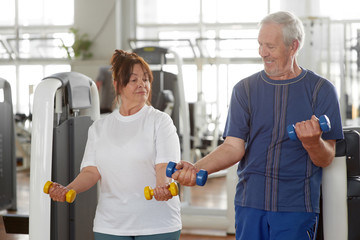 Fototapeta premium Caucasian senior people exercising at gym. Elderly couple lifting dumbbells together at fitness center. People, sport, healthy lifestyle.