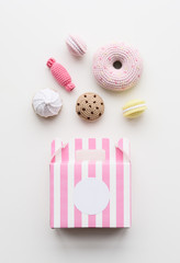 Flatlay of amigurumi toy sweets. Knitted cakes, candies and donuts with pink box on white background