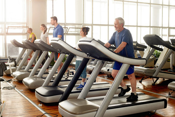 Group of people running on treadmills. People of different ages exercising in fitness center....