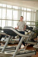 Pretty young woman on treadmill at fitness club. Happy sporty girl with slim body exercising at fitness center.