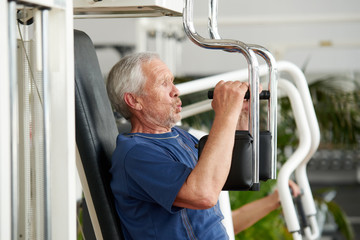 Senior man training on butterfly fitness machine. Side view senior man doing chest exercise on machine at gym. Benefits of strength training for seniors.