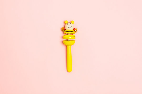 Yellow wooden baby rattle with bells over pink background. Mock up. Copy space. Flat lay style