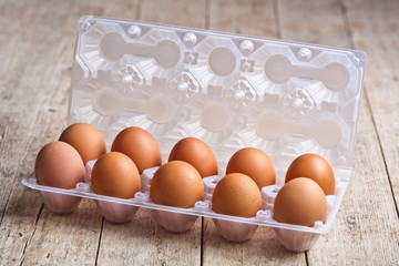 Fresh chicken eggs on plastic container on rustic wooden table.