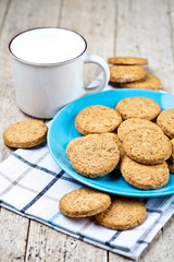 Fresh baked oat cookies on blue ceramic plate on linen napkin and cup of milk.
