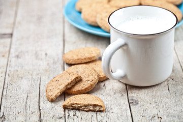 Cup of milk and fresh baked oat cookies on blue ceramic plate on rustic wooden table background.