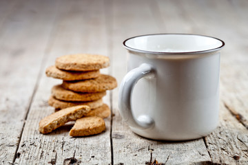 Cup of milk and stack of fresh baked oat cookies on rustic wooden table background. With copy space.
