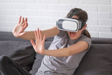 Woman wearing VR goggles. She is afraid and holding her arms in front.