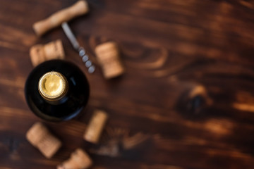 A dark bottle of wine next to blurry a corkscrew and corks on a wooden background.