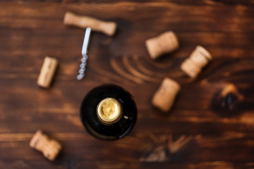 A dark bottle of wine next to blurry a corkscrew and a twisted cork on a wooden background.
