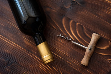 A dark bottle of wine next to a corkscrew on a wooden background.