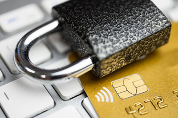 Concept of security of electronic payment. Lock on gold credit card and white keyboard.
