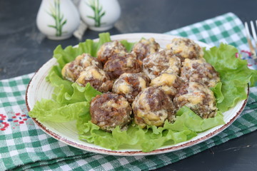 Meatballs in a sauce of cheese and sour cream are located in a plate on a dark background