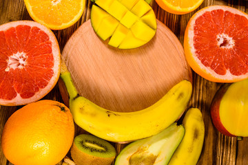 Still life with exotic fruits and cutting board. Bananas, mango, oranges, avocado, grapefruit and kiwi fruits on wooden table. Top view