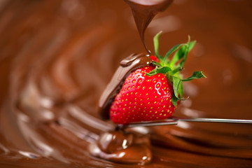 Strawberry in chocolate. Melted chocolate pouring on fresh ripe juicy strawberry closeup over swirl brown background. Fondue. Dessert