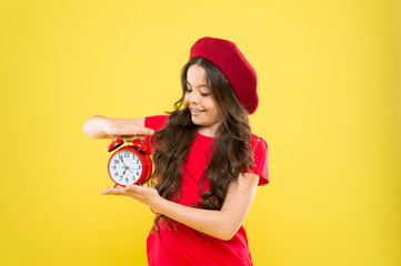 happy girl with long curly hair in beret. child with alarm clock. Timeless fashion. parisian child...