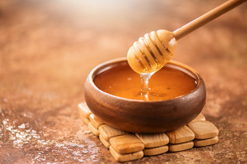 Honey dripping from honey dipper in wooden bowl. Healthy organic thick honey pouring from the...