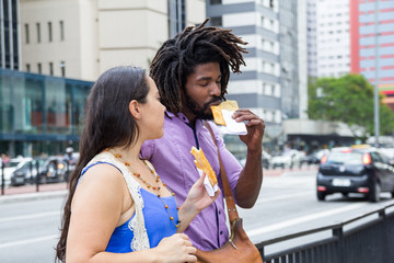 Multiracial couple sharing in the streets brazilian food known as Pastel - asian recipe.