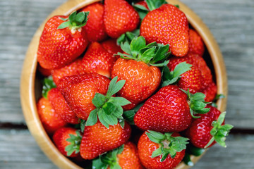 Sweet fresh juicy organic ripe strawberries in wooden bowl on wooden surface outdoors in garden or backyard