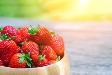 Sweet fresh juicy organic ripe strawberries in wooden bowl on wooden surface outdoors in garden or backyard