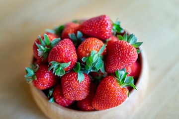 Sweet fresh juicy organic ripe strawberries in wooden bowl on wooden table surface at home