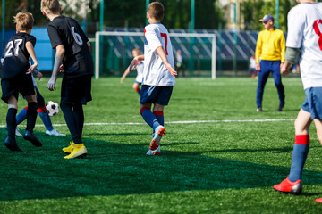 Boys at black white sportswear run, dribble, attack on football field. Young Soccer players with ball on green grass. Training, football, active lifestyle for kids  