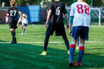 Boys at black white sportswear run, dribble, attack on football field. Young Soccer players with ball on green grass. Training, football, active lifestyle for kids  