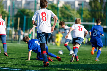 Obraz premium Junior football match. Boys in blue white sportswear play soccer match on football pitch. Football stadium, grass field at the background Soccer for young players. Training, sport, activity outdoor