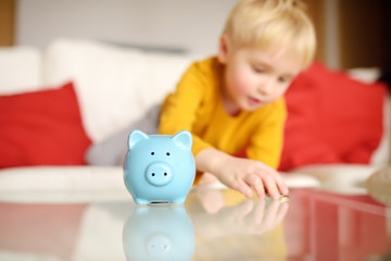 Little boy putting coin into piggy bank.