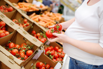Pregnant woman in a food store or a supermarket choosing fresh organic tomatoes