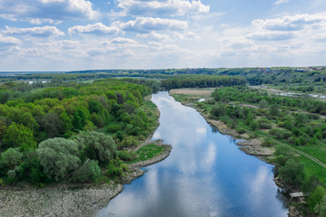 Aerial view of river with reflected blue sky and clouds, green meadows with trees and plants. Beautiful summer nature landscape from above