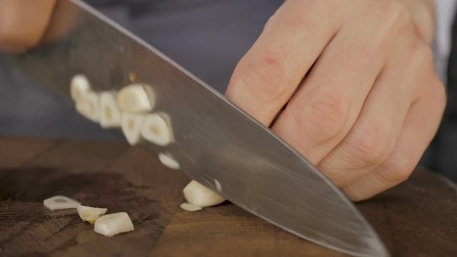 Chef slicing garlic on the cutting board with a knife