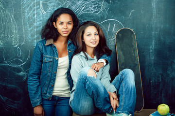 back to school after summer vacations, two teen real girls in classroom with blackboard painted together, lifestyle mixed races people concept close up
