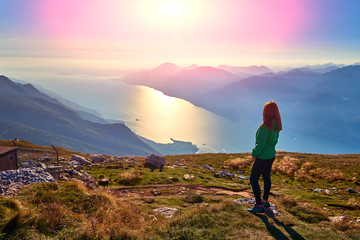 Fototapeta premium A beautiful woman admiring the beautiful Lake Garda on Monte Baldo, Panorama of the gorgeous Garda lake surrounded by mountains