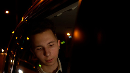 Portrait of young handsome teenager traveling in a taxi car with a driver in night city