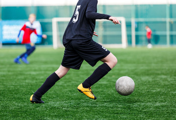 Boys at black red sportswear run, dribble, attack on football field. Young soccer players with ball on green grass. Training, football, active lifestyle for kids  