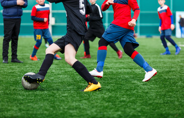 Boys at black red sportswear run, dribble, attack on football field. Young soccer players with ball on green grass. Training, football, active lifestyle for kids  