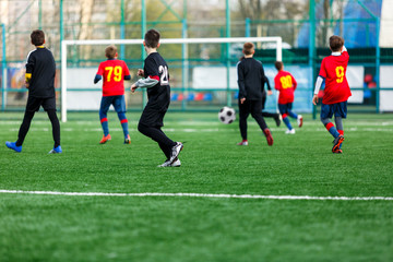 Boys at black red sportswear run, dribble, attack on football field. Young soccer players with ball...