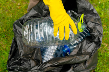 Hand putting empty plastic bottle into a black plastic trash bag.