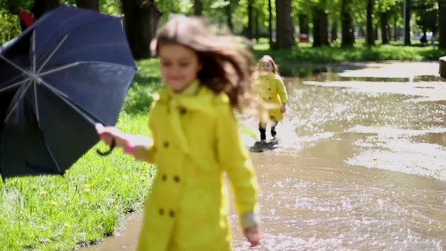 Two girls playing and running through puddles in the park during a sunny day