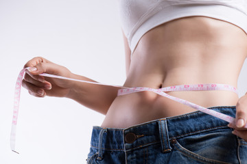 Close up slim young woman measuring her thin waist with a tape measure. Healthcare and woman diet...
