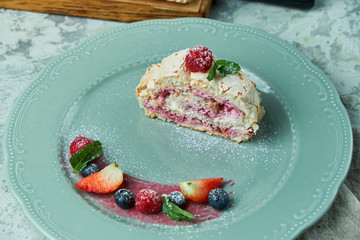 Meringue cake roll slice on a plate with berries, on a gray background